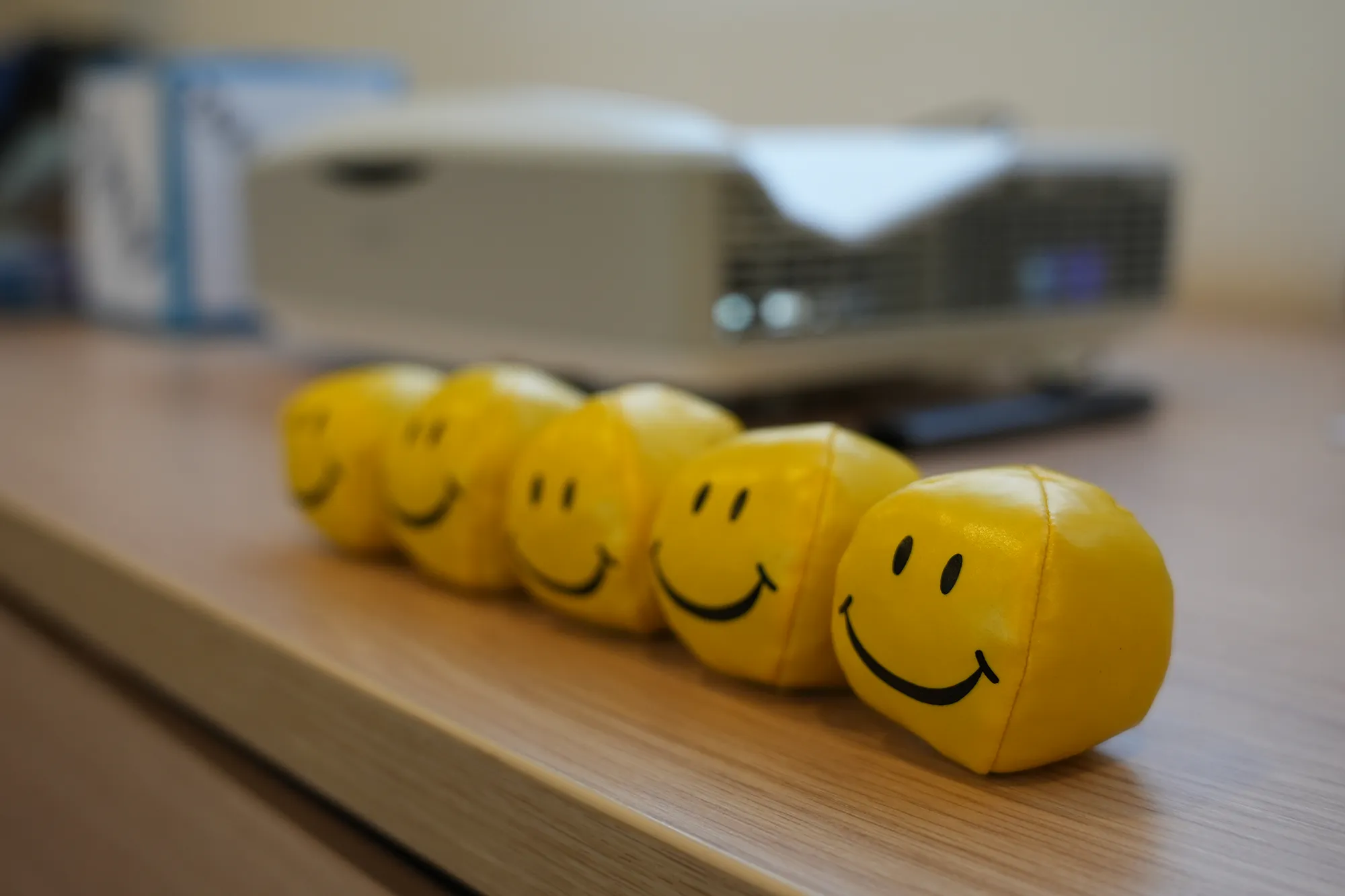 Fünf gelbe Smiley-Bälle stehen auf einem Holztisch