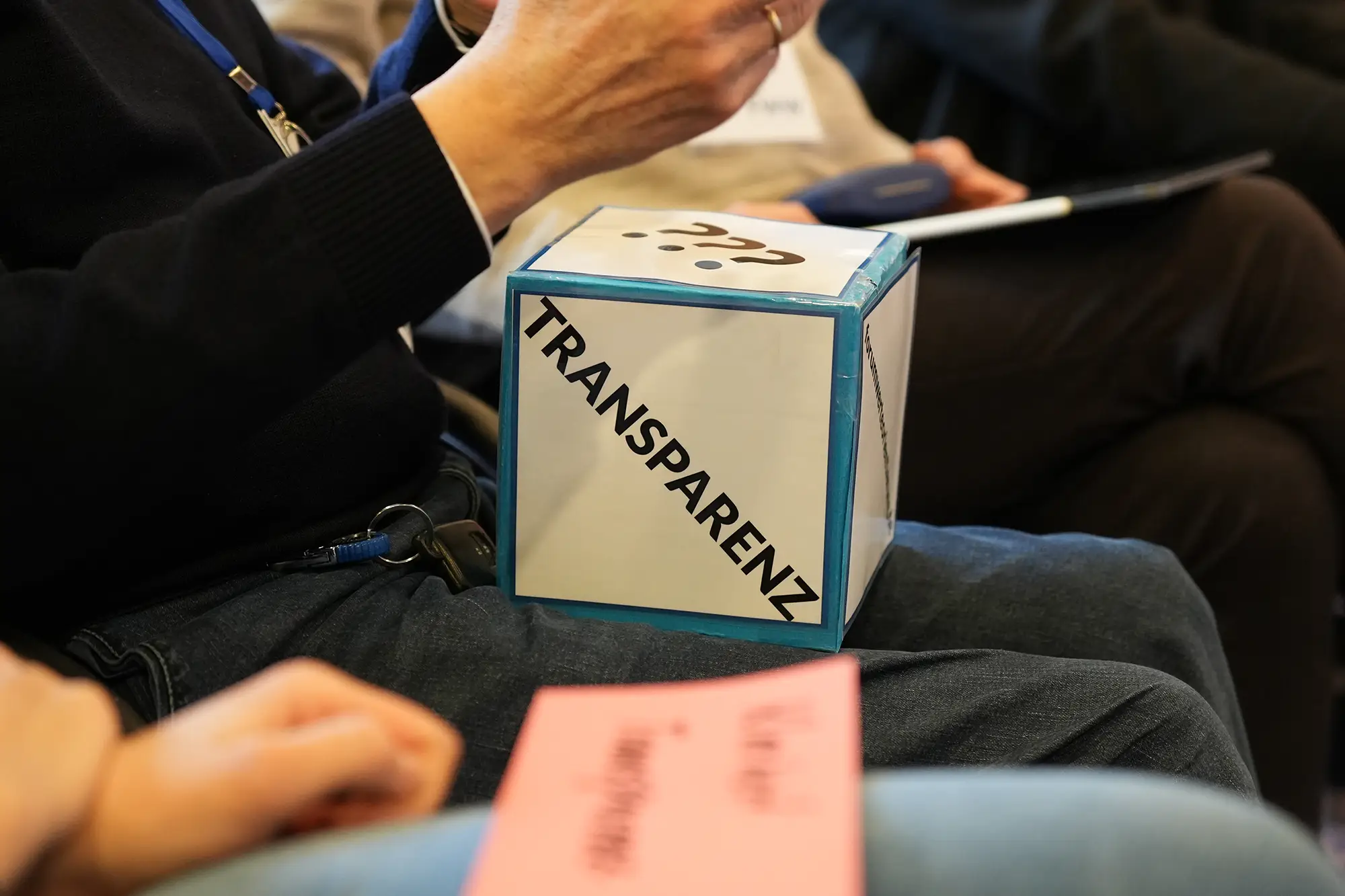 Person hat einen Würfel mit dem Schriftzug "Transparenz" auf dem Schoss